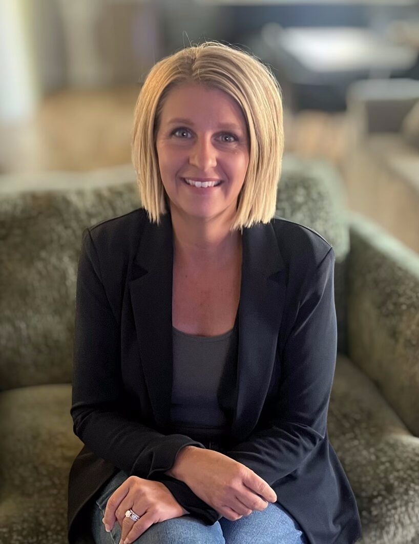 Cortney, Design Consultant at Blinds by Valeri, smiling while seated on a cozy green sofa, showcasing her approachable "Midwest Nice" design philosophy.